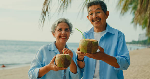 istock Asian elderly cheerful couple smile looking at camera and drinking coconut on beach enjoying the sea view. A happy senior adult people enjoy the travel lifestyle after retirement. 2158674827