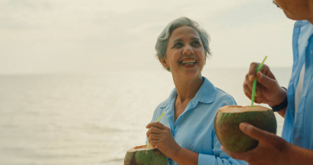 istock Asian elderly cheerful couple drinking coconut while walking on beach enjoying the sea view. A happy senior adult people enjoy the travel lifestyle after retirement. 2158674829
