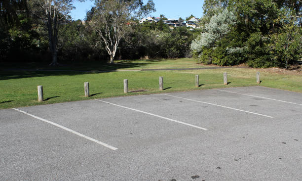 istock Empty parking lot with marked spaces next to a park with trees and grass 2158675438