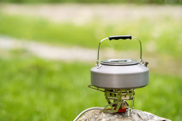 Boiling water with kettle at camping site, camping and adventure concept