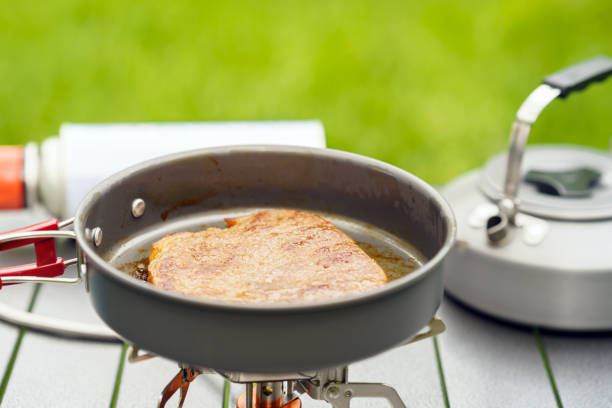 Frying steak in pan at camping site, camping and adventure concept