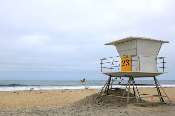Lifeguard tower stands on a pristine sandy beach under a clear blue sky, facing the calm, vibrant blue ocean. Minimalistic, summery, and tranquil atmosphere perfect for relaxation or coastal themes