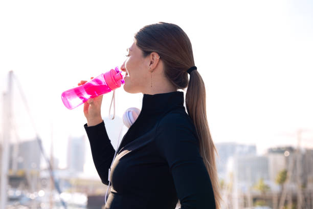 istock Side view runner girl drinking water from a sports bottle outdoors.Vertical 2158686848