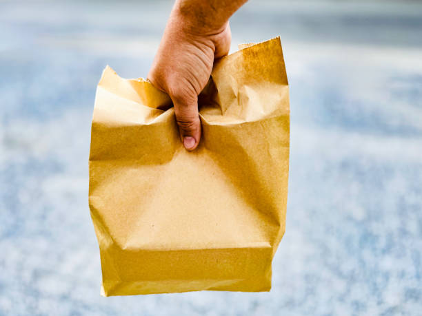 A person's hand is holding a paper bag, possibly containing items from a deliveryservice.