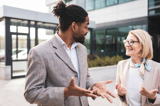 istock Two professional colleagues having a joyful conversation outside a modern office building. They appear engaged and relaxed, representing positive workplace interaction and communication. 2158699600