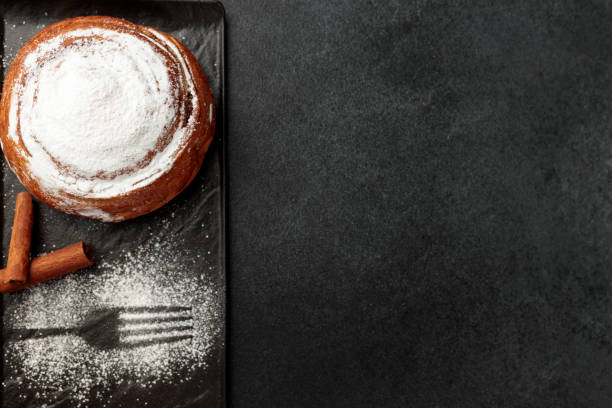 istock Round, delicious bun with cinnamon and powdered sugar on a black plate on a gray background 2158700341