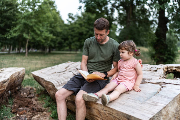 istock Father and daughter reading a book in the park 2158705072