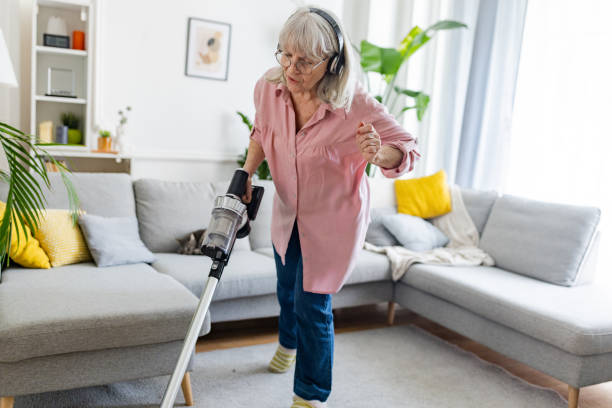 Senior woman engaged in household chores, vacuuming her living room while transported to another world through her headphones.