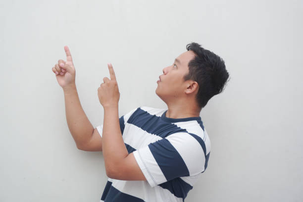istock Asian male with t-shirt pointing, isolated on white background. 2158708288