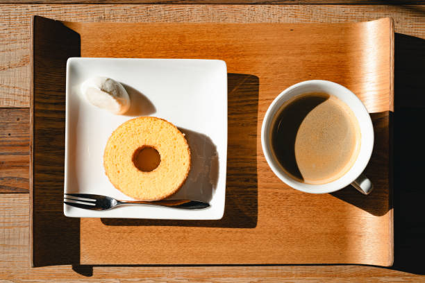 A serving of freshly brewed coffee and a slice of Baumkuchen on a white plate with a fork, accompanied by a small confectionery. The setup is placed on a wooden tray, capturing the essence of a simple yet elegant breakfast.