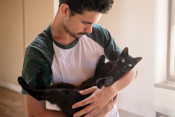 istock young man holds a black cat in his arms 2158714690