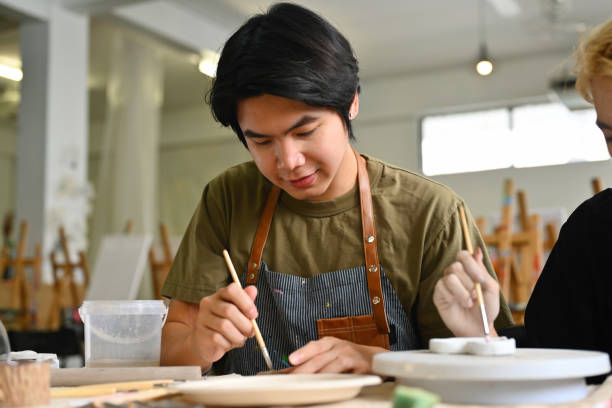 istock An art student paints a ceramic piece with focused concentration, Crafts and DIY with people concept 2158716524