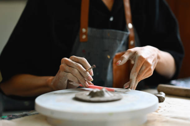 istock A person working on a pottery wheel, shaping clay with both hands and using a sculpting tool. They wear an apron, focusing intently on the clay piece in progress, Crafts and DIY with people concept 2158716758