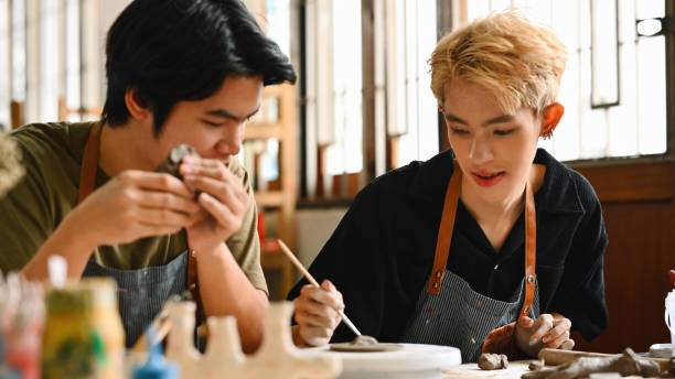 istock Two young men are engaged in pottery making. One carefully sculpts a clay piece, while the other adds details with a tool. Both wear aprons and focus intently on their creative work 2158717690