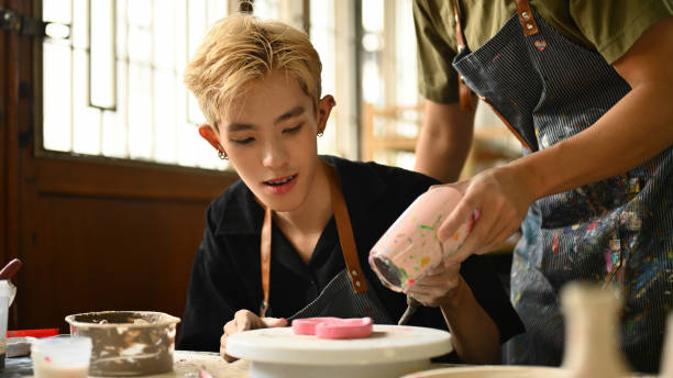 istock An instructor uses a hair dryer to help an LGBT student dry a painted ceramic piece. Both are focused and engaged in the creative process in a well-equipped, bright studio, Crafts and DIY concept 2158717991