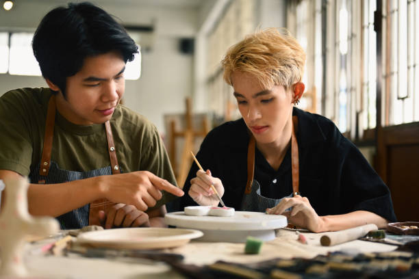 istock An art instructor guides an LGBT student as they paint a ceramic piece. Both are focused in a bright studio filled with pottery tools and materials, fostering a supportive learning environment 2158718622