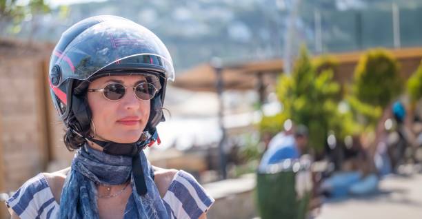 Beautiful woman wearing a motorcycle helmet on a summer day, smiling and looking on a motorcycle.