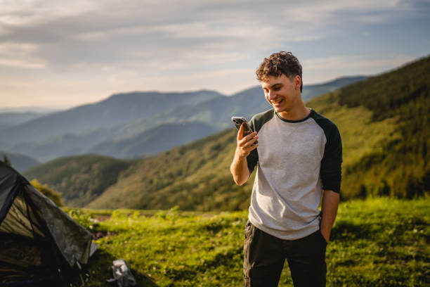 Young boy stand in front tent and use mobile phone on the mountain