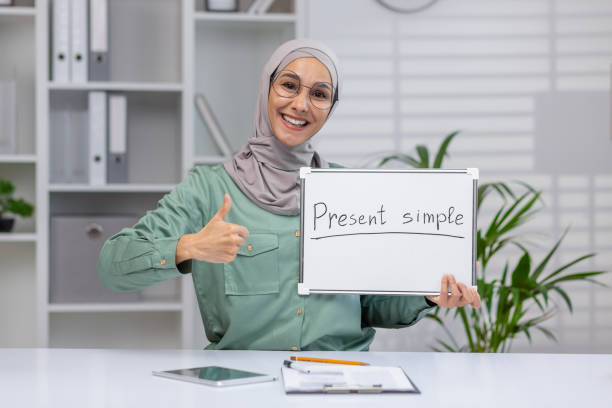 istock Smiling teacher showing present simple on whiteboard in classroom while giving a thumbs up 2158723232