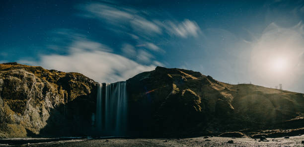 istock Night view of Skogafoss waterfall in Iceland, illuminated under a starry sky with dramatic cliffs and flowing clouds. 2158723307