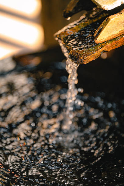 Close-up image capturing water flowing from a wooden spout into a natural pool. Sunlight illuminating the scene creates reflections on the water surface, adding a serene and tranquil ambiance.