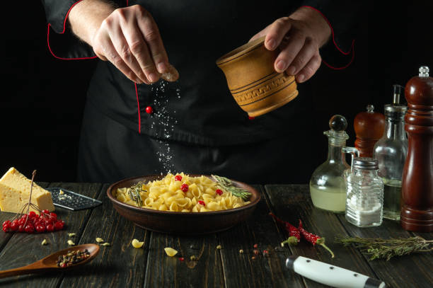 The chef adds salt with his hands to a bowl of pasta on the kitchen table. Low key concept of preparing a delicious lunch at the inn