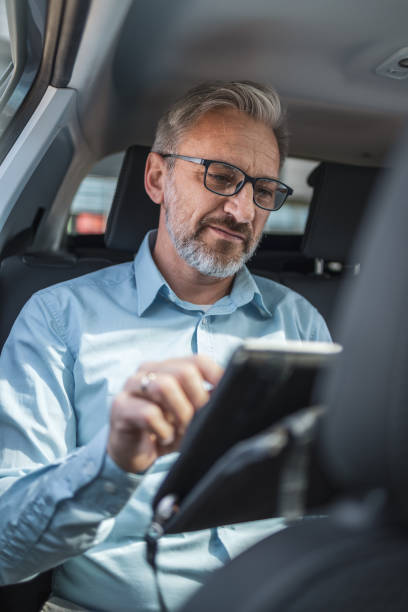 istock A mature businessman working remotely on a digital tablet while commuting in the backseat of a car. This image captures the essence of modern business travel and remote work. 2158728967