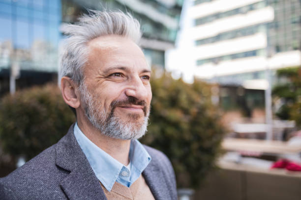 istock A mature businessman with a gray beard smiling while commuting outdoors. The backdrop consists of modern city buildings. The image captures a feeling of confidence and satisfaction. 2158729046