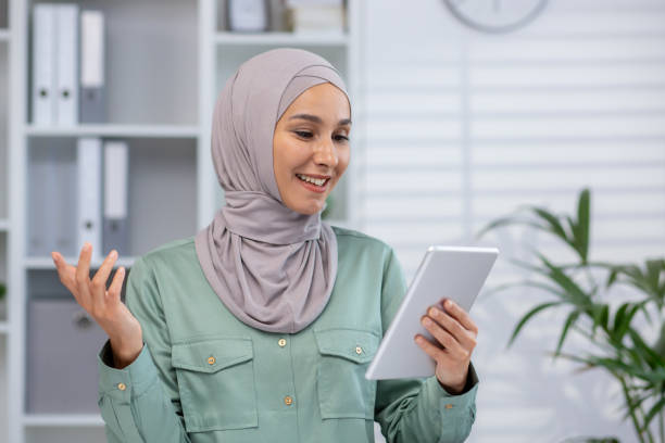 istock Smiling woman in hijab using tablet in modern office setting 2158729051
