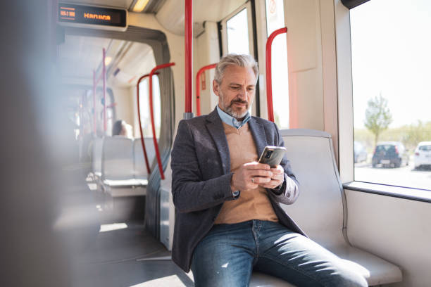 istock A mature man working remotely on his smartphone while commuting on a train. He is dressed in casual business attire, focused and productive amidst his commute. Concepts include remote work, commuting, and business travel. 2158729053