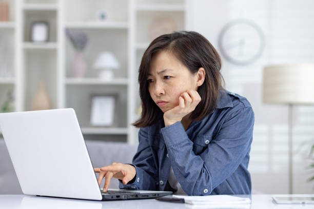 istock Focused Asian woman working from home on laptop, showing determination and concentration 2158732420