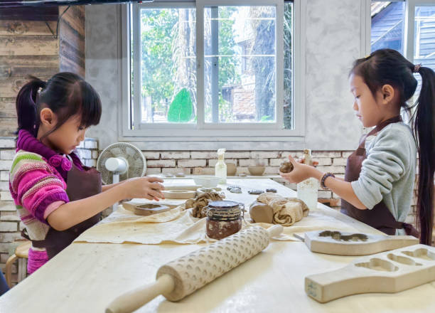 Two Asian girls kneading clay in the pottery classroom,  they wearing aprons to prevent their clothes from getting dirty