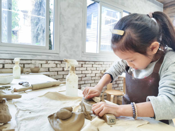 An Asian girl kneading clay in the pottery classroom,  she wearing aprons to prevent their clothes from getting dirty