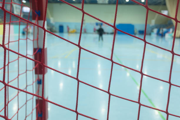Pre-adolescent boys and girls wearing blue and green scrimmage vests and celebrating a goal while playing ball indoors.