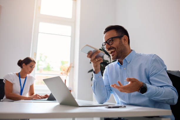istock Cheerful businessman using mobile phone and talking on the speaker in the office. 2158752428