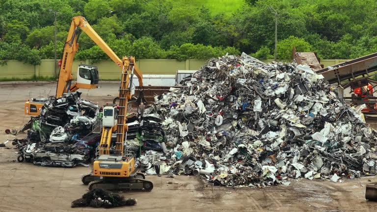 Old vehicle utilization junkyard with claw crane manipulator machines lifting and disposing cars for scrap metal. Transport equipment at crashed auto disposal site