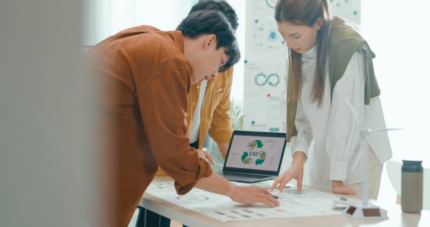 Team members examine ESG-related documents, pointing and discussing investment strategies for sustainable and renewable energy resources. Eco-Friendly Business Team Discussing ESG Goals.