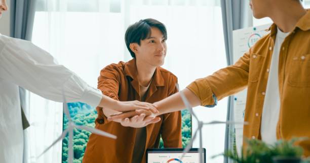 Diverse team unites hands over desk with renewable energy models, symbolizing cooperation and agreement on sustainable business practices.Eco-Friendly Business Team Discussing ESG Goals.
