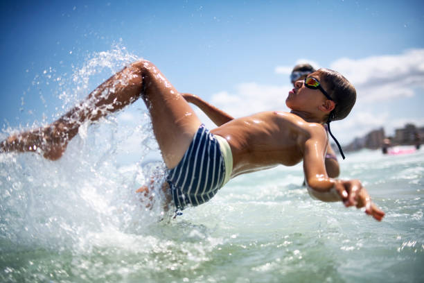 A blonde boy plays in the sea waves with a swimming board