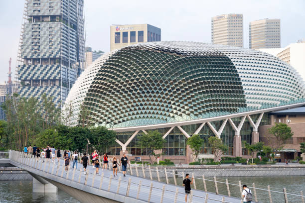 Singapore, Singapore - April 3, 2024. People walking on bridge over river with Esplanade Theatres on the Bay in downtown Singapore