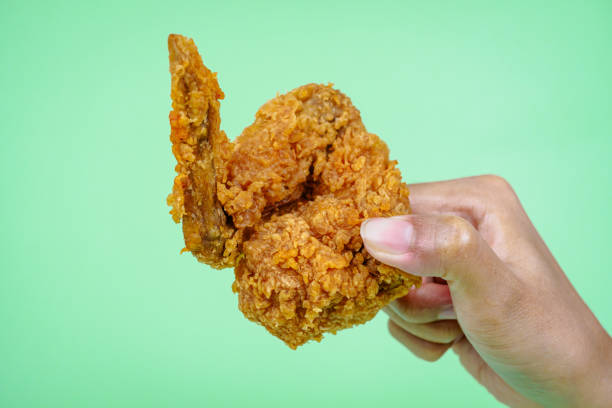 istock Female hand holding fried chicken on green background. 2158768541