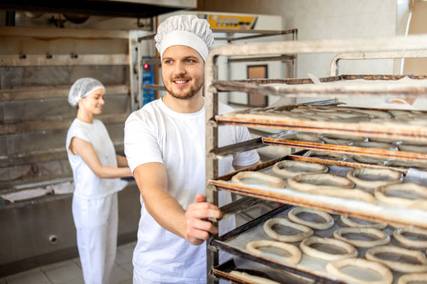 istock Male baker moving tray of dough rings in bakery. 2158773092