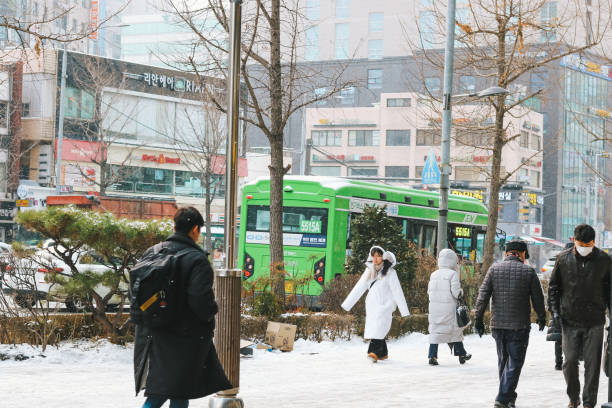 People walking wearing long padding during heavy snowing in downtown. Seoul snowy street. Gwanak-gu, Seoul, South Korea - December 20, 2023: People walking wearing long padding during heavy snowing in downtown. Seoul snowy street. seoul bus stock pictures, royalty-free photos & images
