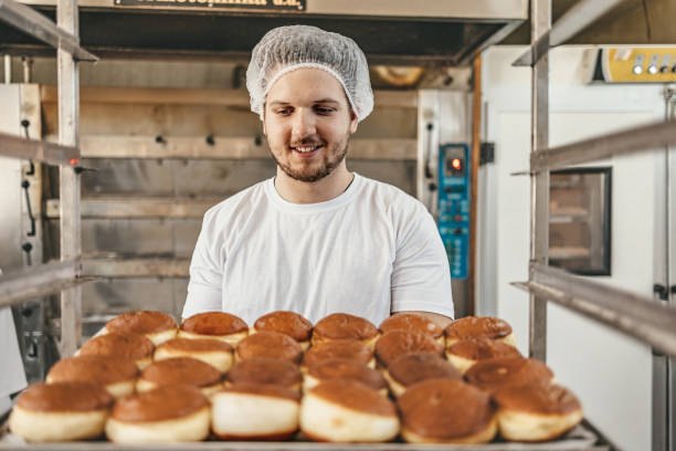 istock Baker holding tray of freshly baked pastries in bakery kitchen 2158773225
