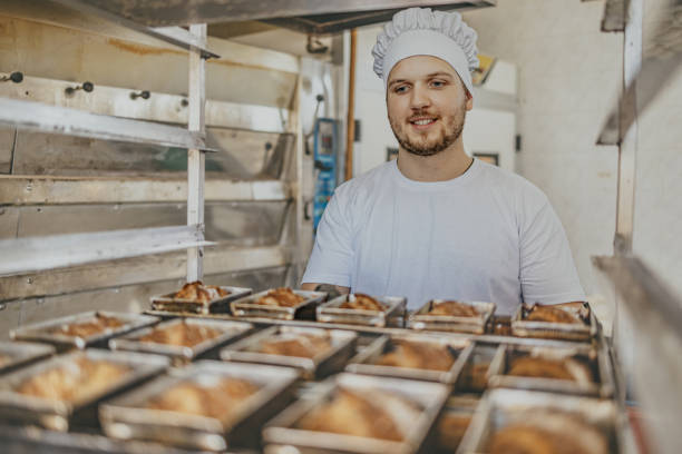istock Baker in white hat inspecting freshly baked bread in a commercial bakery 2158773246