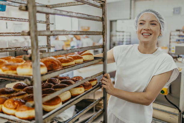 istock Smiling baker arranges freshly baked doughnuts on cooling racks in a busy bakery 2158774189