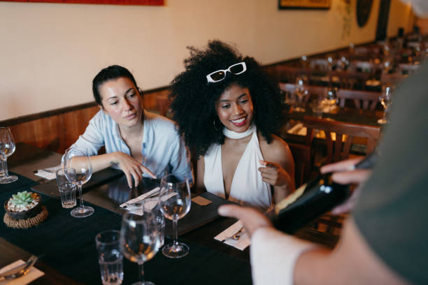 istock Two Young Women Ordering Red Wine from a Waiter in a Restaurant 2158774347