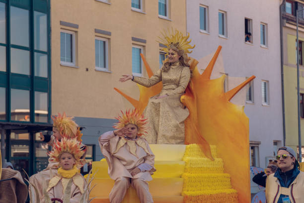 Eisenach, Germany - 09 Mar 2024: Carnaval in German city. A holiday dedicated to saying goodbye to winter and welcoming spring. Beautiful woman and children in yellow costumes riding on a carriage down the street.
