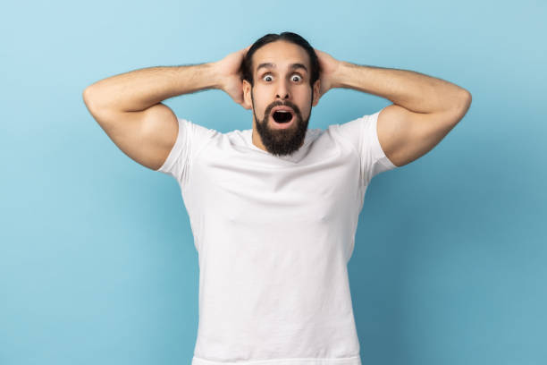 istock Man standing with mouth open in surprise, has shocked expression, keeping hands on head. 2158789298