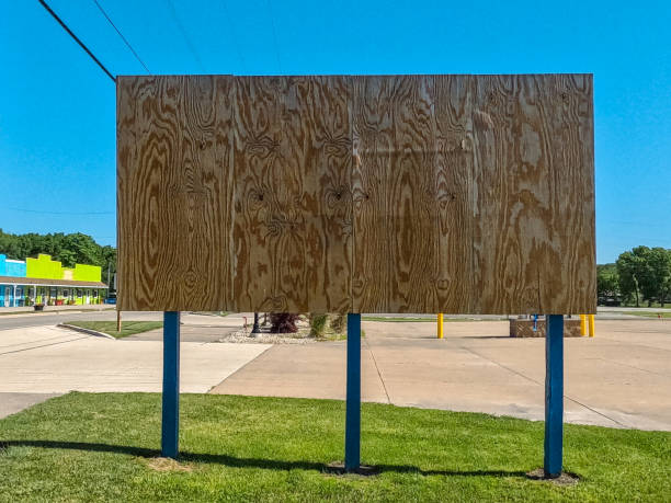 Blank wooden billboard in a small town. A small strip mall is the in the background of view. Clear blue skies overhead.
